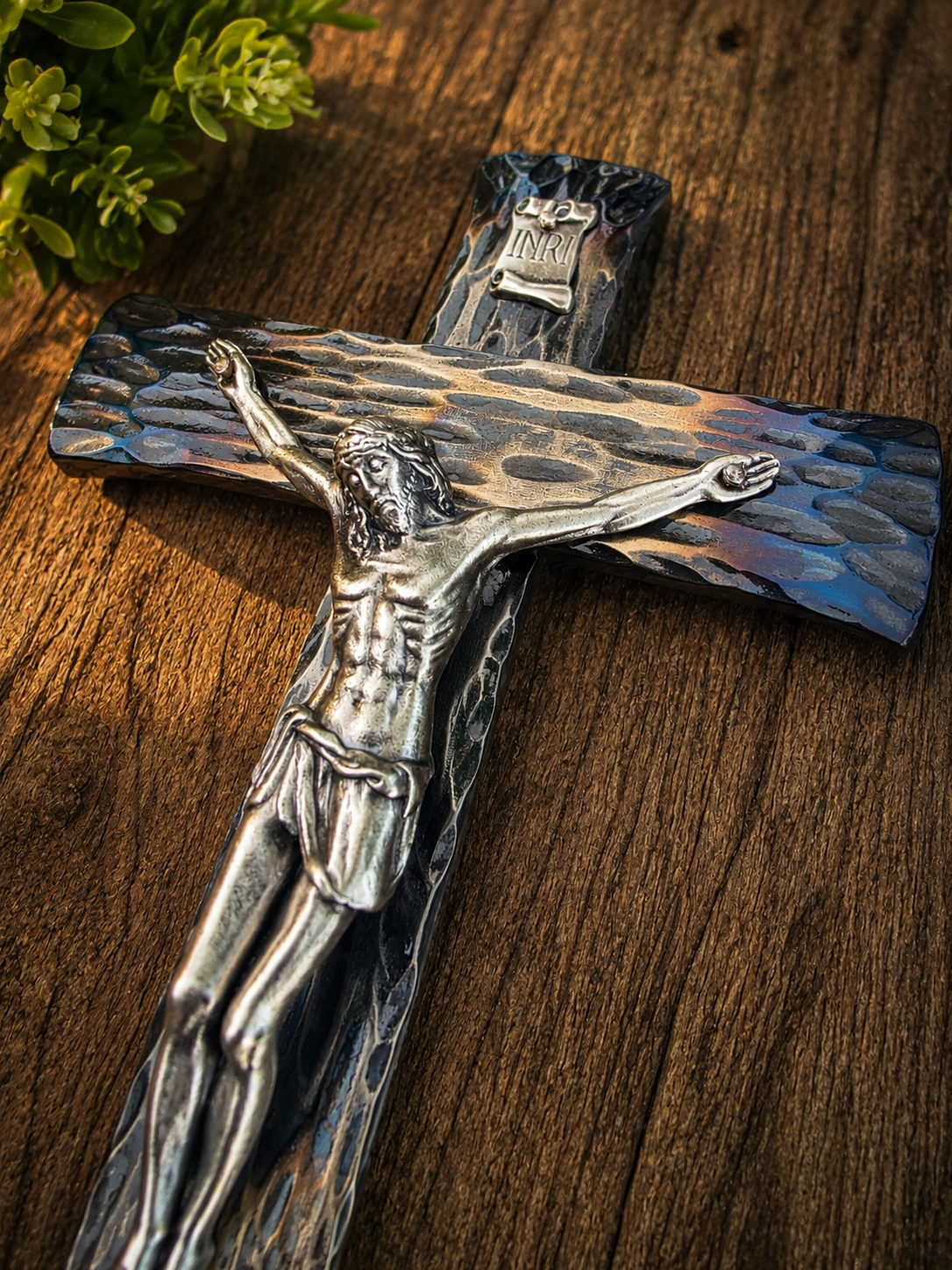 Hand-forged steel wall crucifix displayed on a warm wood wall, highlighting its handcrafted finish and timeless Catholic design.